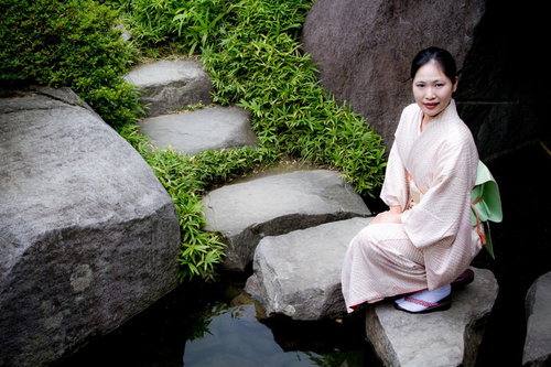 日本庭園の池の踏石にしゃがみこむ着物の女性