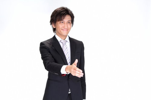 水色の壁の前で笑顔で手を差し出し握手を求めるスーツの男性