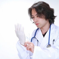 白い壁の前でゴム手袋を手にはめる若い医師の写真