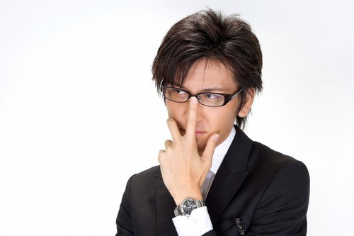 水色の壁の前で眼鏡のフレームに手を当てるビジネスマン