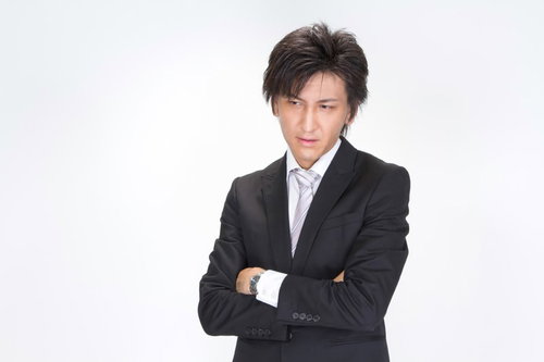 水色の壁の前で腕を組んで立つスーツ姿のビジネスマン