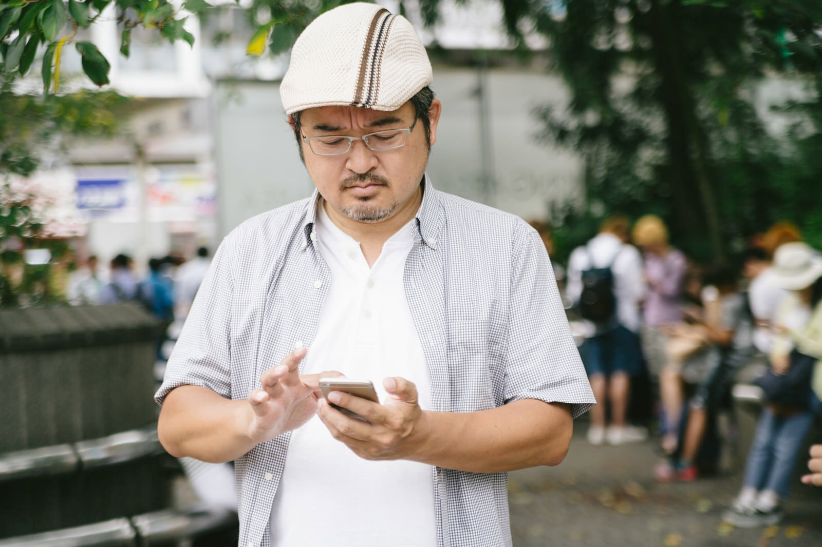 屋外でスマートフォンを両手で操作するハンチング帽の男性［モデル：ナリシゲ］