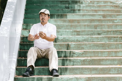 スマホを操作するハンチング帽姿の男性が階段で休憩