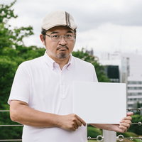 タブレットを持ちながら見解を述べるハンチング帽の男性の写真