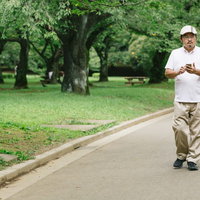 公園内でスマートフォンを片手に探索する男性の写真