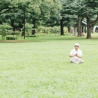 息抜きに公園の芝の上でスマホゲームをプレイする男性の写真