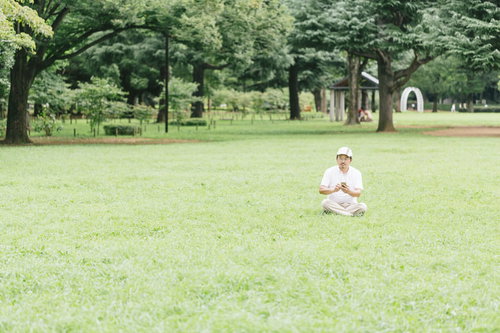 息抜きに公園の芝の上でスマホゲームをプレイする男性