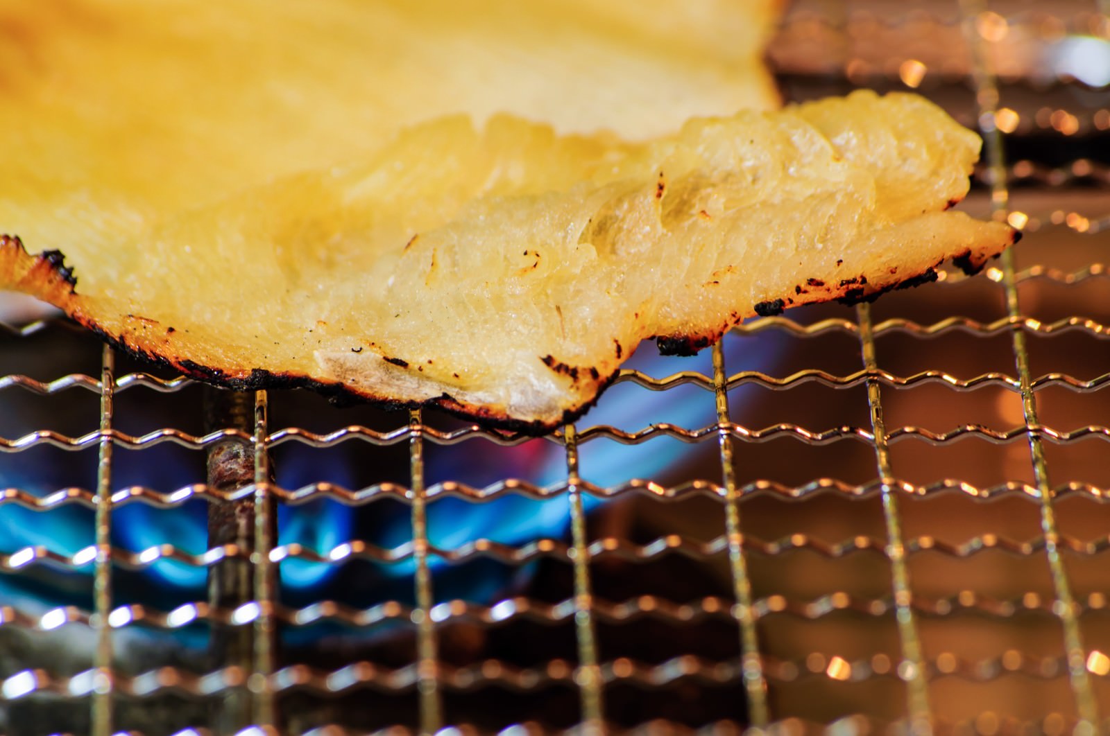 青い炎の上の金網で焼かれるエイヒレの網焼き