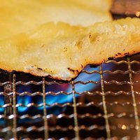 青い炎の上の金網で焼かれるエイヒレの網焼きの写真