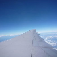 旅客機の翼の向こうに青空と白い雲が広がる機窓からの風景の写真