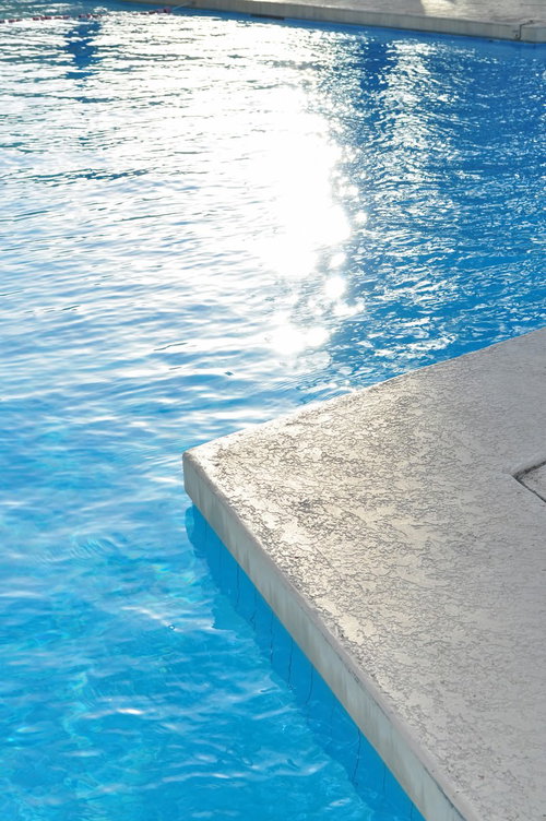 青い水面と白いデッキチェアが並ぶプールサイドの風景