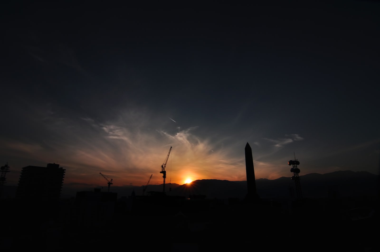 建設クレーンのシルエットと山の端に沈む夕日