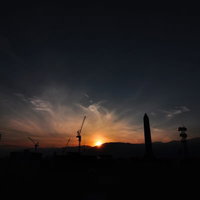 クレーンのシルエットと山の端に沈む夕日の写真