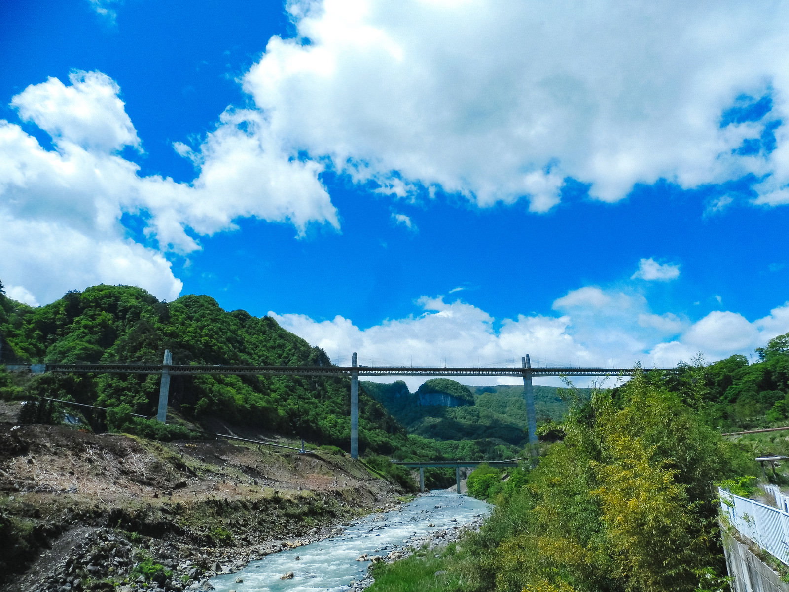 青空の下、吾妻川沿いにそびえ立つ丸岩の絶壁と奥に架かる橋