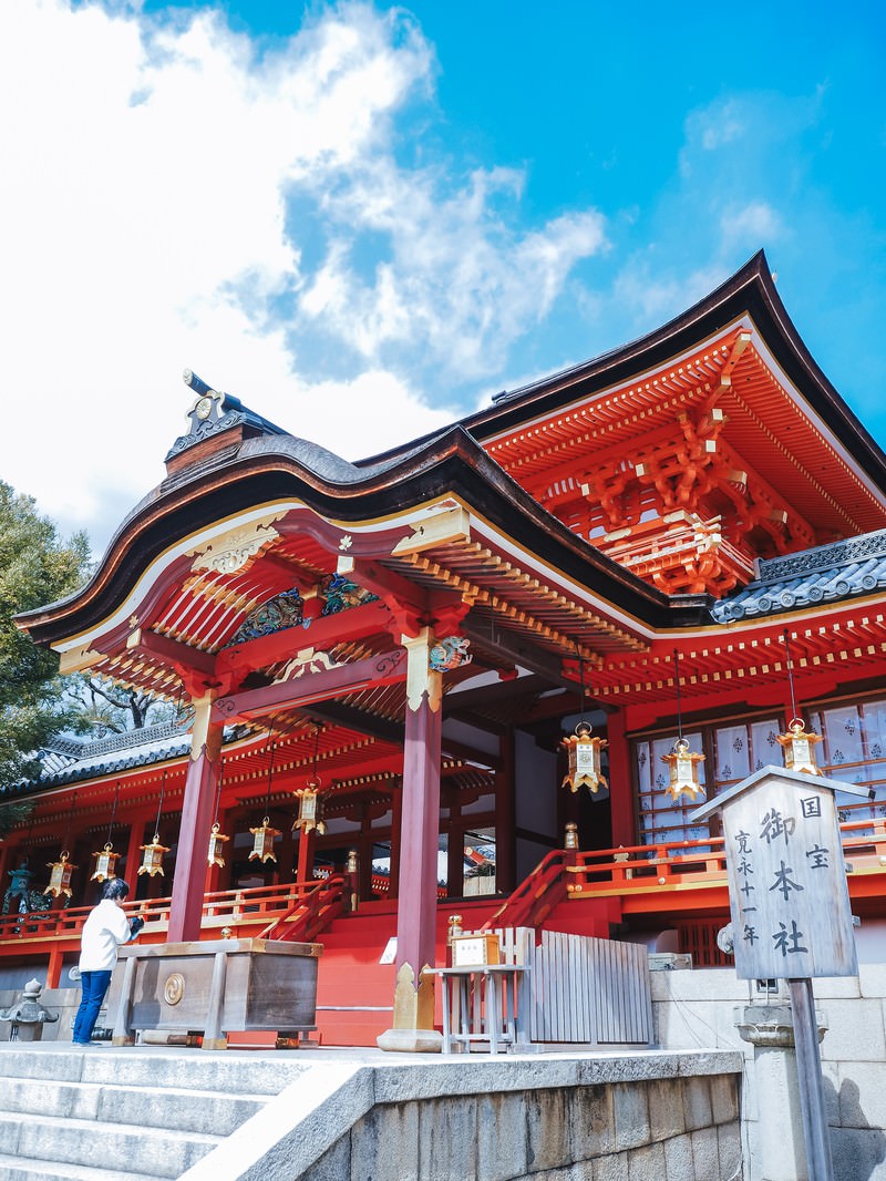 朱色の石清水八幡宮本殿前で参拝者が手を合わせている境内の風景