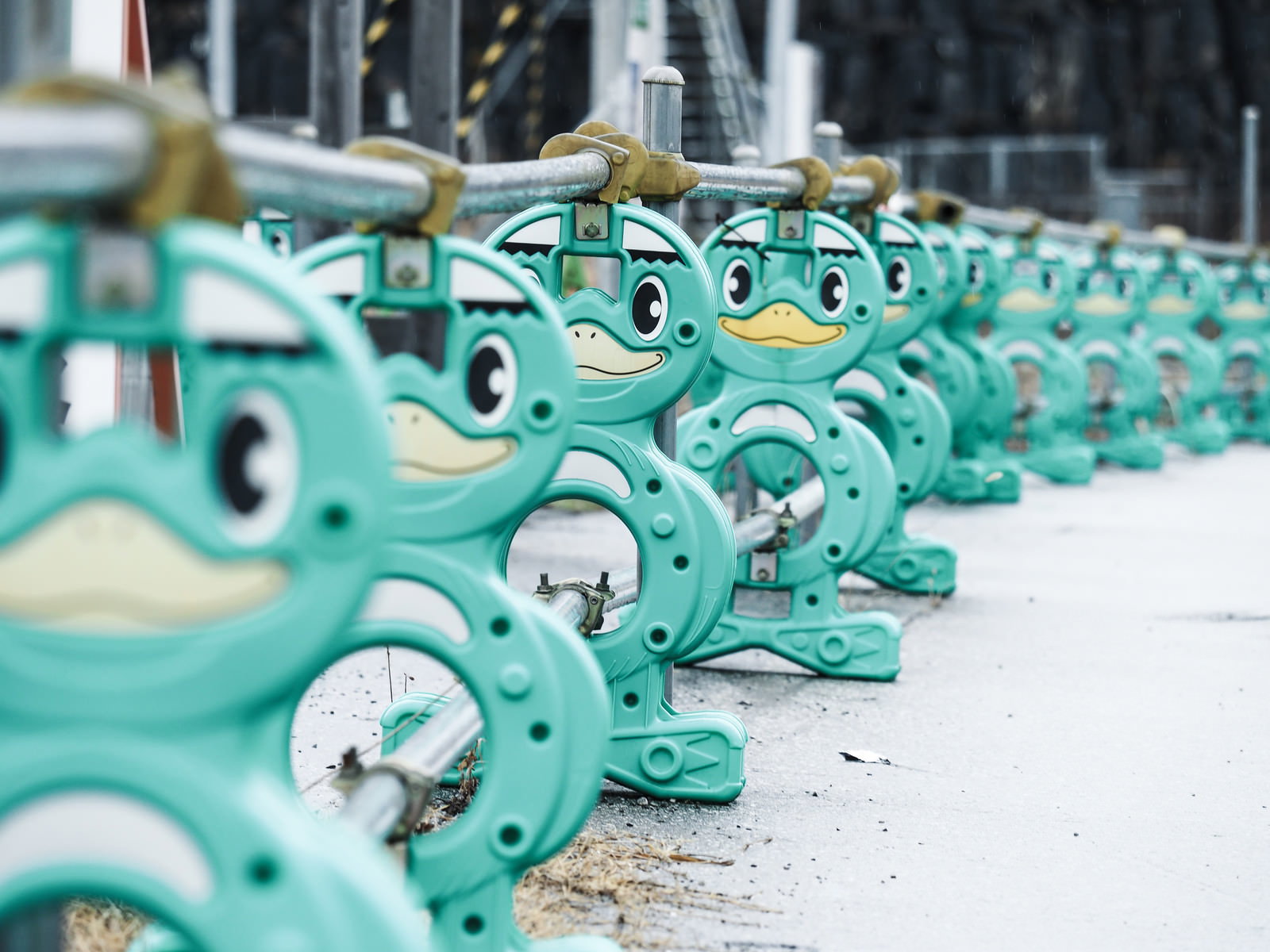 工事現場に設置された緑色の河童型バリケードが単管パイプで連結されている