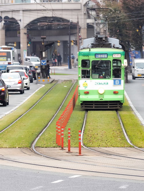 緑化された軌道を走る熊本市電の路面電車と都市景観