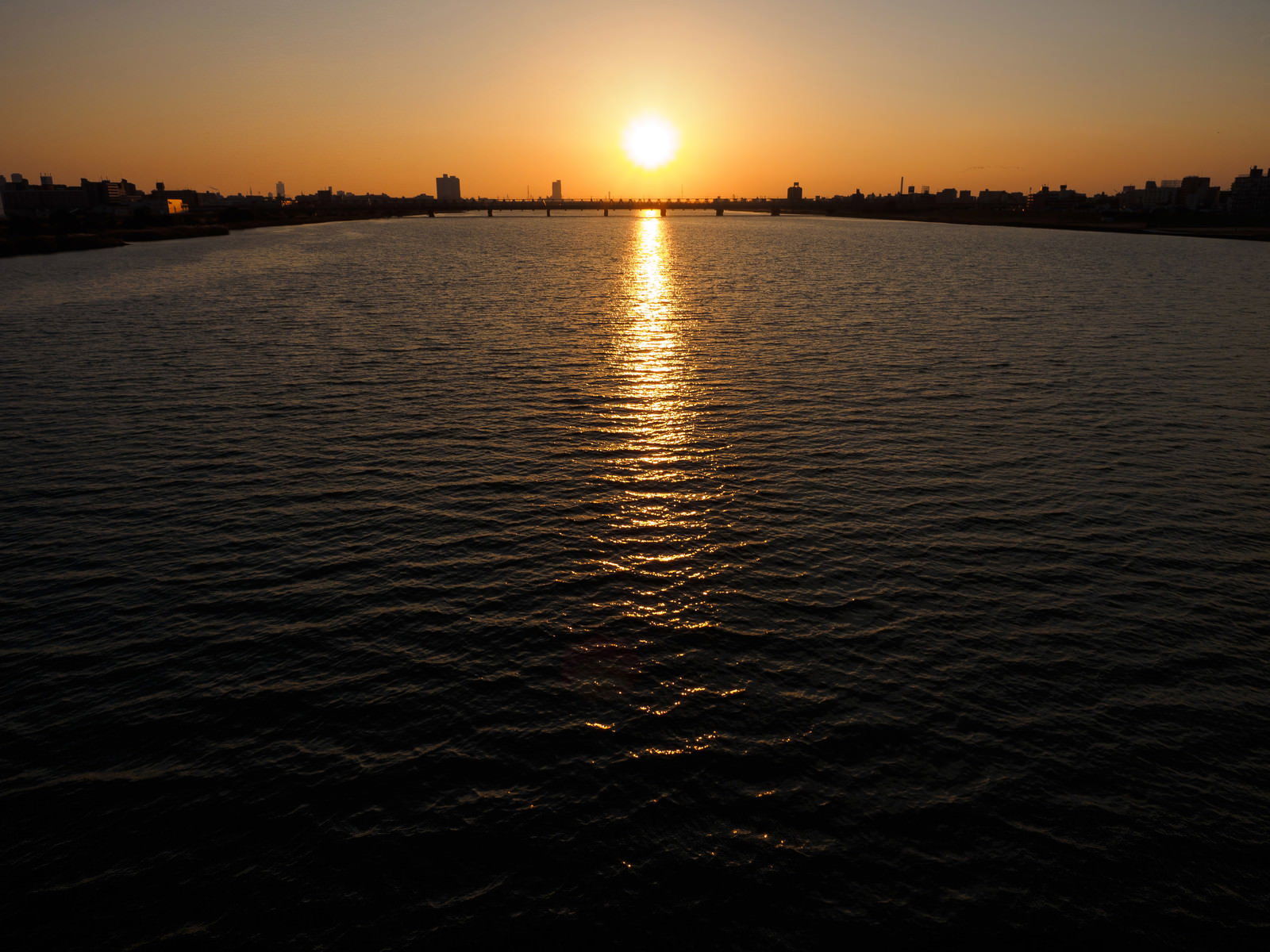 夕焼けの河川に映る太陽と両岸の街並み
