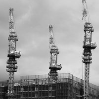 建設中のビルに並ぶ3台のクレーンと鉄骨造りの建設現場の写真