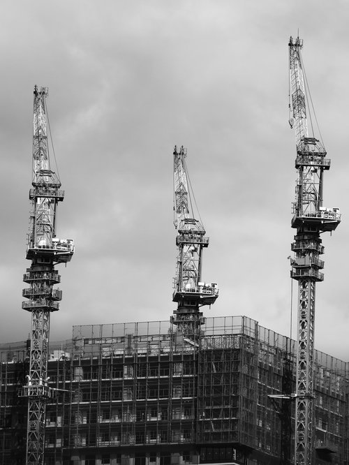建設中のビルに並ぶ3台のクレーンと鉄骨造りの建設現場
