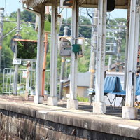 ローカル線の駅ホームで待つ爽夏、青いベンチに座る女性の写真