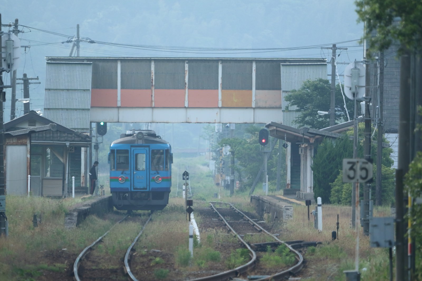曇り空の下、駅構内を走る青い電車