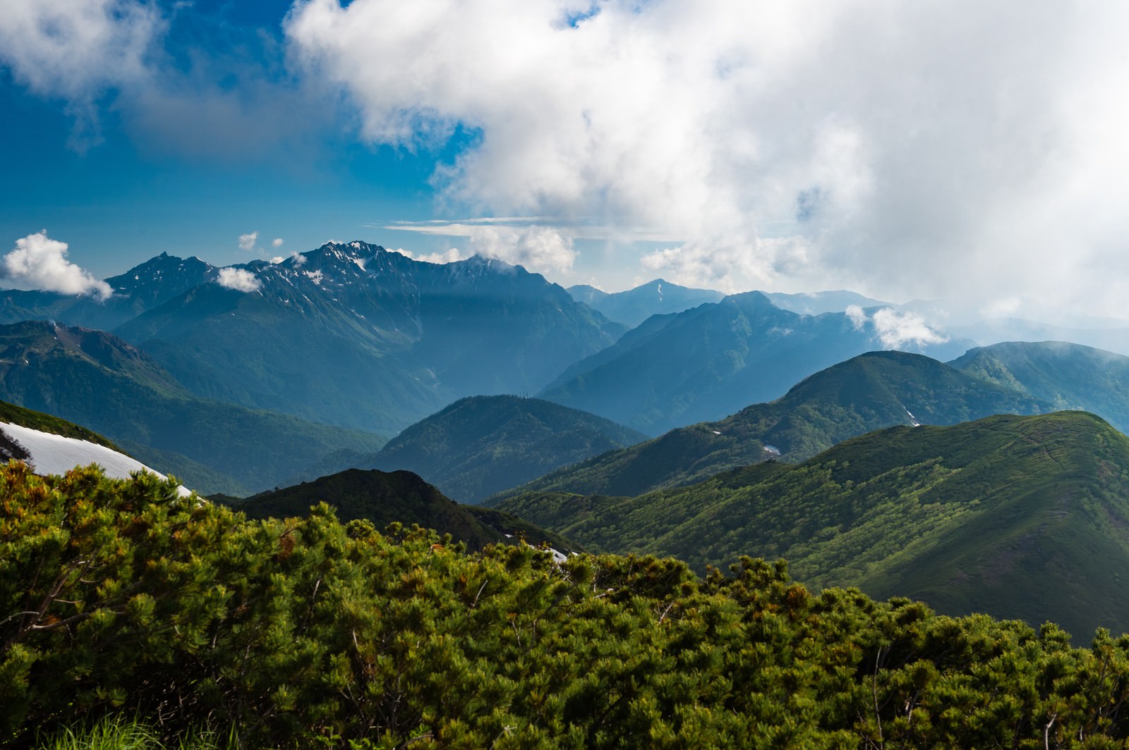 青空の下に緑の山々と雪山が連なる乗鞍新登山道の風景