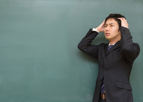 黒板の前で両手で頭を抱えて悩み込む塾の講師