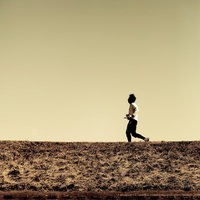 夕暮れのオレンジの空を背景に河川敷を走るランナーのシルエットの写真