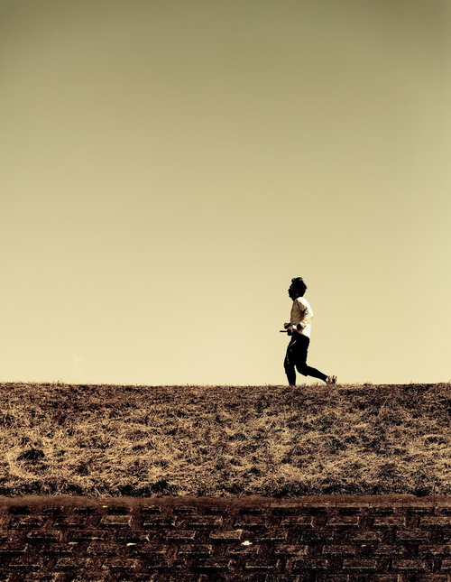 夕暮れのオレンジの空を背景に河川敷を走るランナーのシルエット