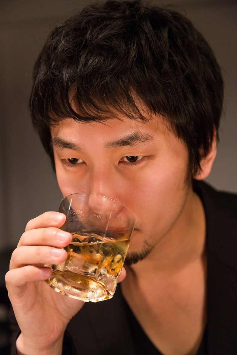 グラスでウイスキーを飲む黒い服の男性［モデル：大川竜弥］