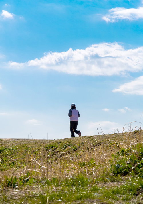 夕方の河川敷をジョギングするランナーの横姿