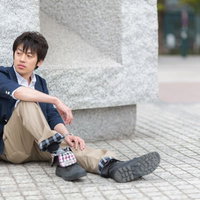 コンクリートの地面に膝を立てて座り物思いにふける青年の写真