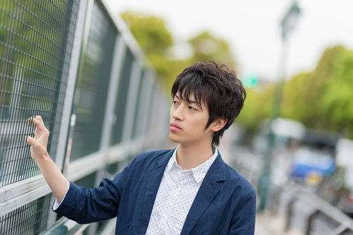 金網のフェンスを両手で握りしめてこちらを見る青年