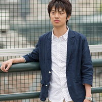 金網フェンスに寄りかかって腕を組みポーズする男性の写真