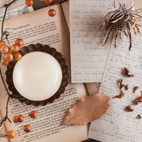 ロウソクの灯りに照らされた古い本や瓶が並ぶ魔女の机の写真