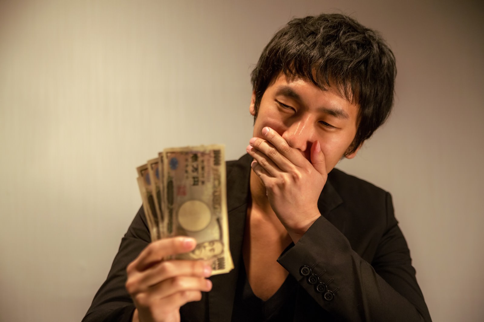 紙幣を持ちながら口を押さえて驚く男性［モデル：大川竜弥］