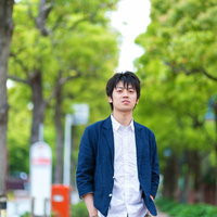 緑のトンネルのような並木道を歩く青年の後ろ姿の写真