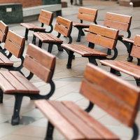 公園の木陰にきれいに等間隔で並んだ木製ベンチの写真