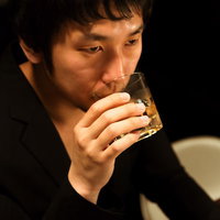 グラスを傾けてウイスキーを口にする大人の男性の写真