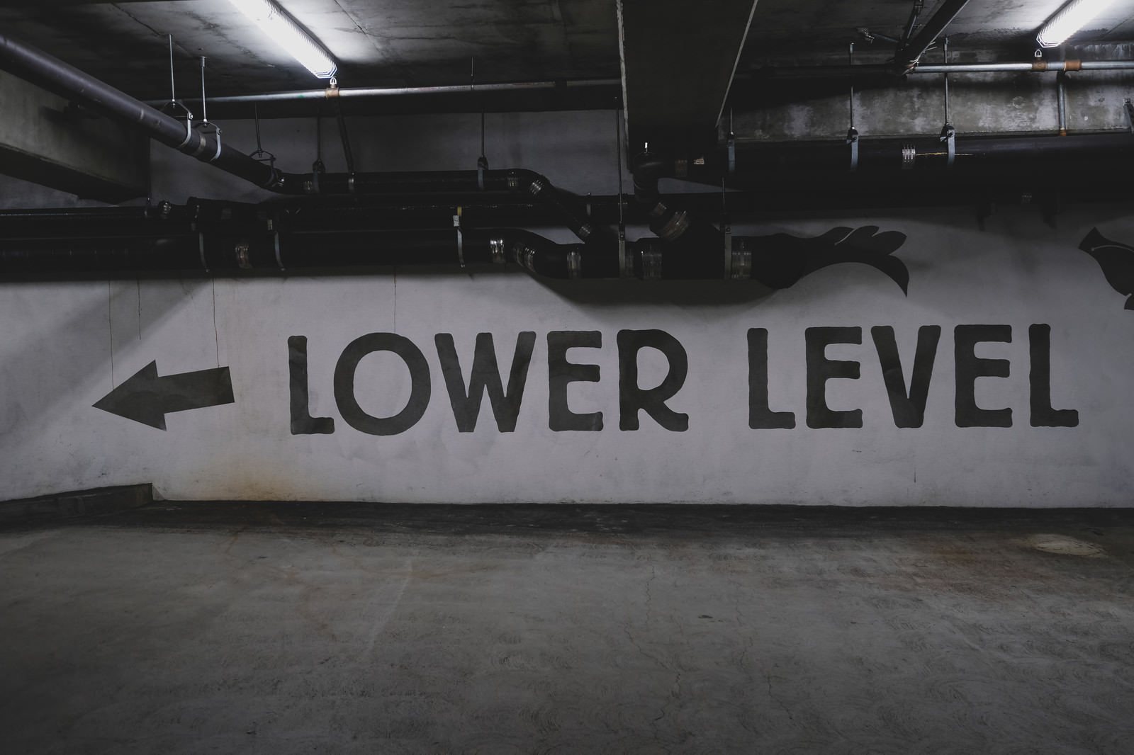地下駐車場の白い壁に黒文字でLOWER LEVELと左向き矢印が書かれた案内標識