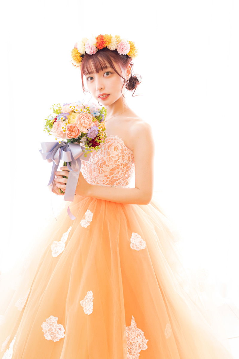 オレンジ色のウェディングドレスを着た花嫁が花を持ってポーズを取っている［モデル：高尾実生］