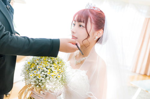 手鏡を見ながら化粧直しをする花嫁のウェディングドレス姿