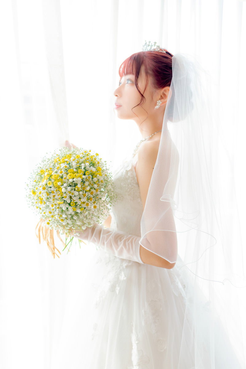 白いウェディングドレスを着た花嫁が黄色い花のブーケを持って立っている［モデル：高尾実生］