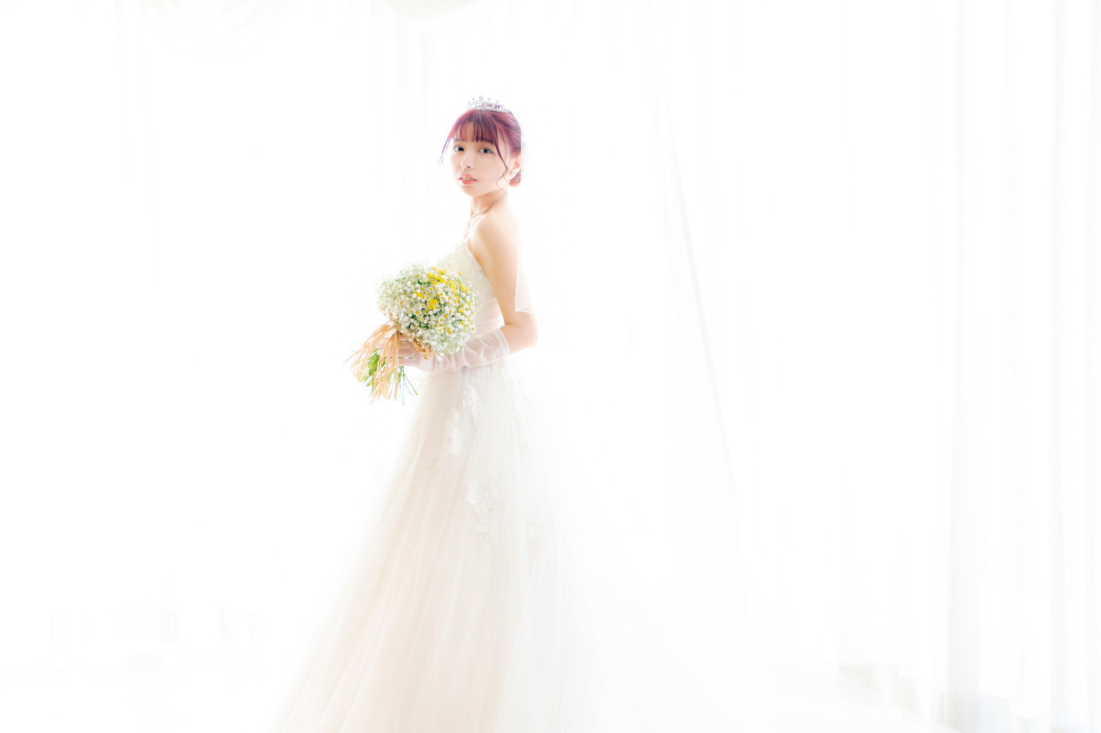 純白のウェディングドレスを着た花嫁が白い背景で立っている［モデル：高尾実生］