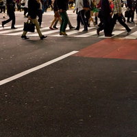 白い横断歩道を行き交う人々の足元と影の写真