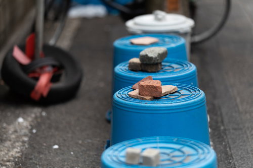 飛ばされないように石が置かれた青いバケツが路上に並ぶ