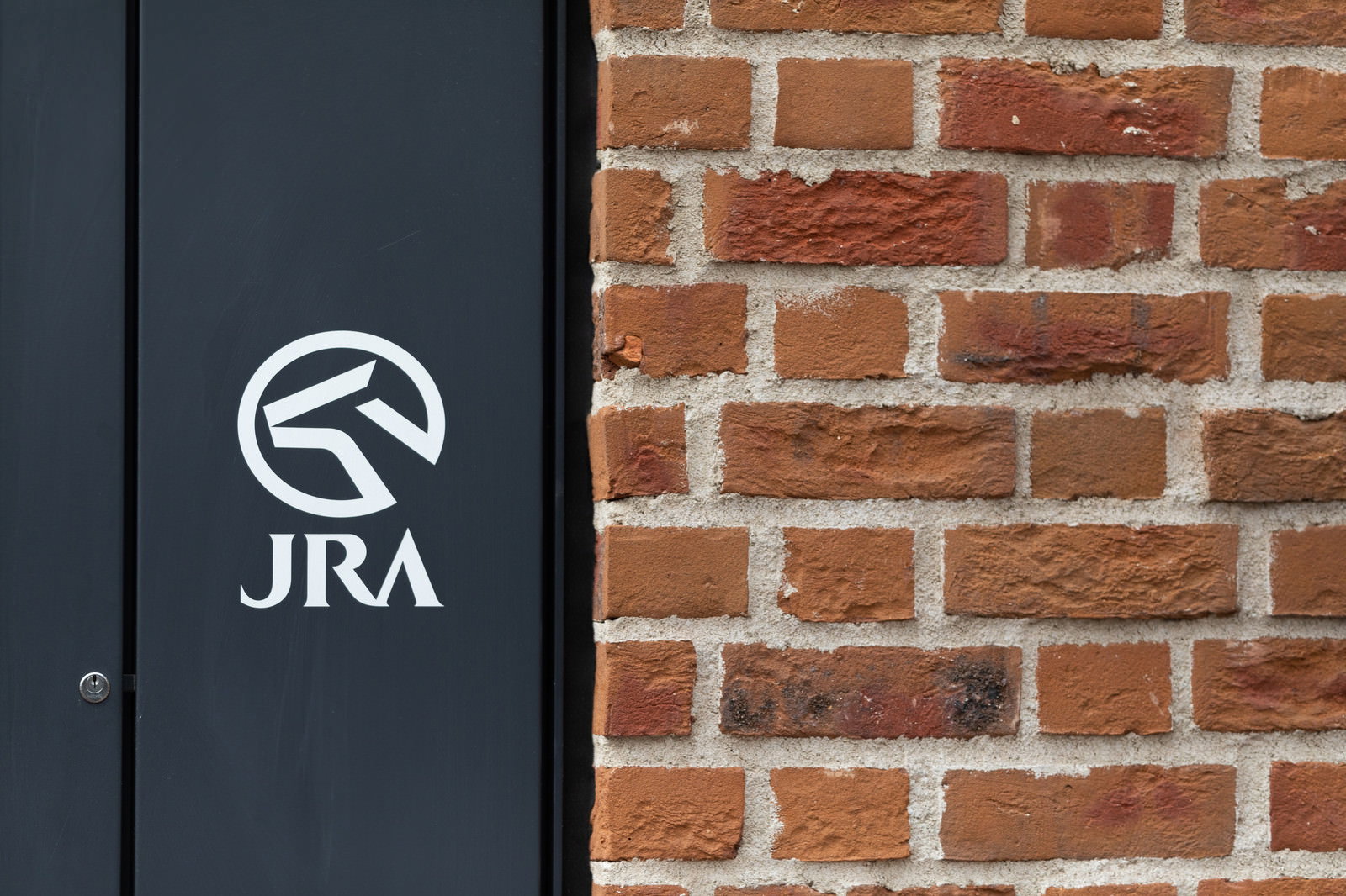レンガの壁に描かれたJRAの白いロゴマーク