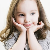 両手に顎を乗せて微笑むブロンドヘアの幼い女の子の写真