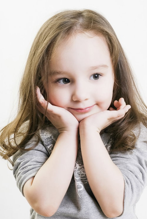 両手に顎を乗せて微笑むブロンドヘアの幼い女の子